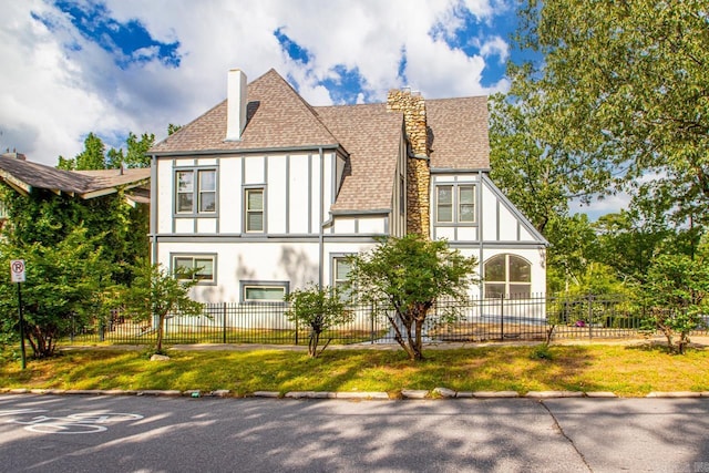 english style home with board and batten siding, a fenced front yard, a chimney, a shingled roof, and stucco siding