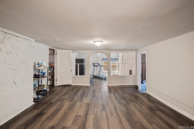 interior space with dark wood-type flooring, arched walkways, a textured ceiling, and baseboards
