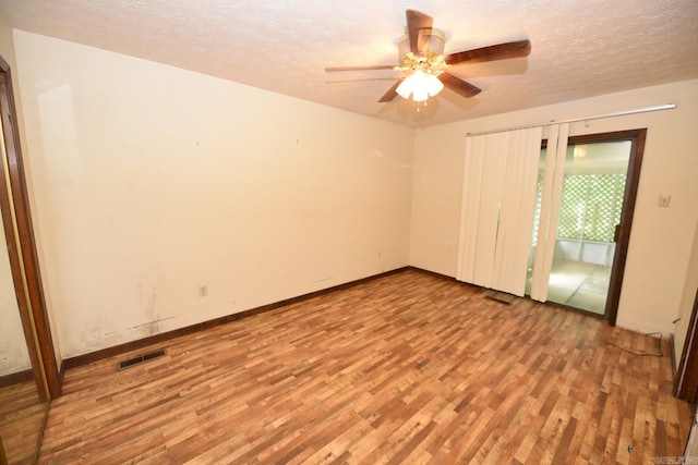 spare room featuring visible vents, wood finished floors, baseboards, a textured ceiling, and a ceiling fan