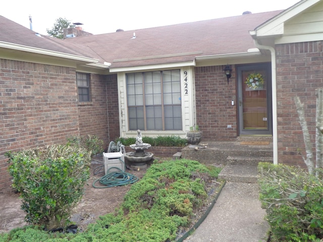 doorway to property with brick siding, a shingled roof, and a chimney