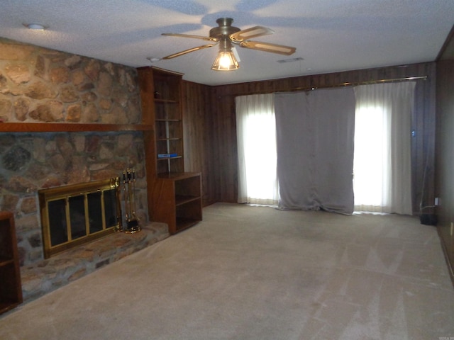 unfurnished living room featuring a stone fireplace, carpet flooring, a ceiling fan, and a wealth of natural light