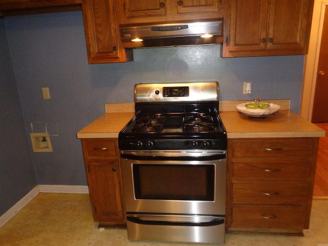 kitchen featuring brown cabinetry, baseboards, range hood, stainless steel range with gas cooktop, and light countertops