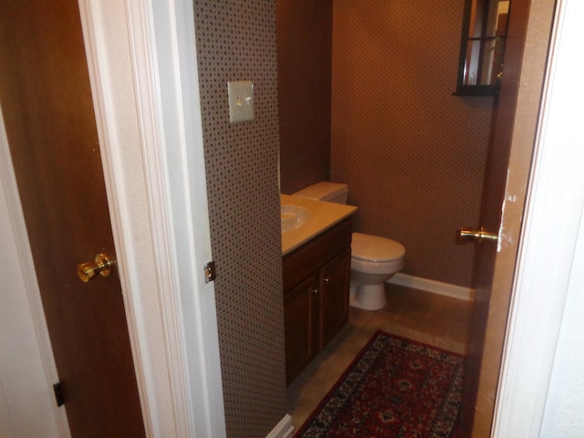 half bath with toilet, baseboards, and vanity