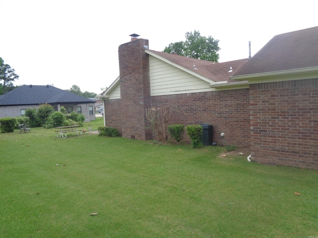 view of side of home featuring brick siding, a yard, and a chimney