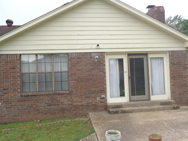 rear view of property with a chimney and brick siding