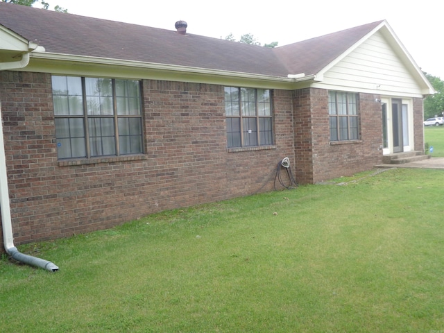 view of side of property with brick siding, roof with shingles, and a yard