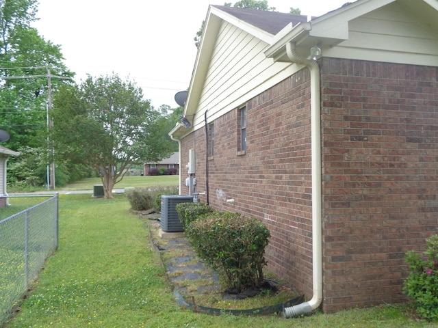view of property exterior featuring central air condition unit, brick siding, a yard, and fence
