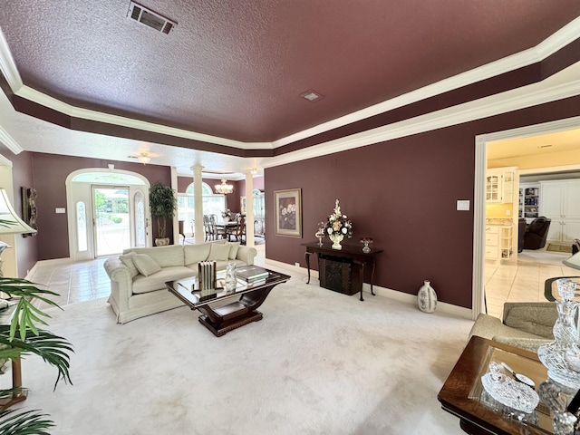 carpeted living room with visible vents, crown molding, arched walkways, a raised ceiling, and ornate columns