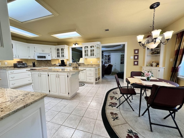 kitchen with white microwave, light tile patterned flooring, a notable chandelier, glass insert cabinets, and white cabinetry
