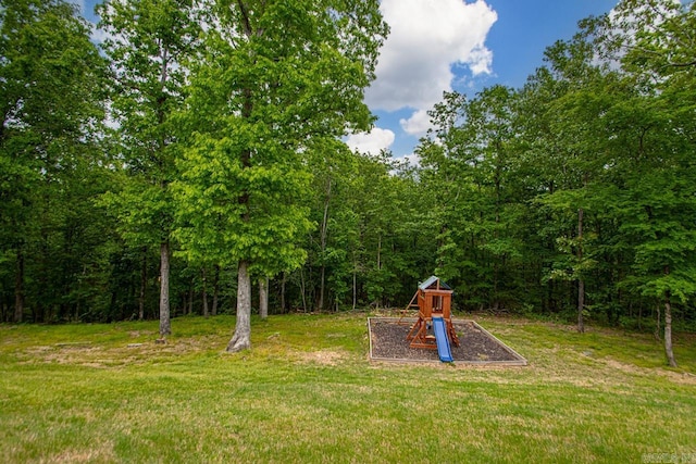 view of jungle gym featuring a lawn and a forest view