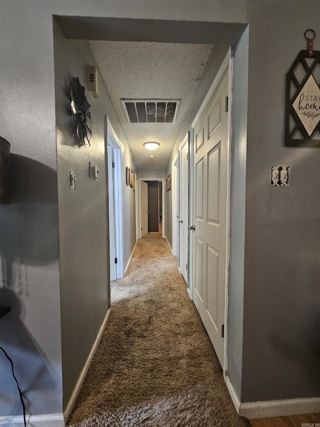 hallway featuring a textured ceiling, visible vents, baseboards, and carpet floors