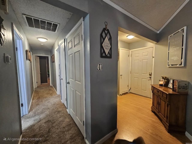 hall with a textured ceiling, visible vents, baseboards, and ornamental molding