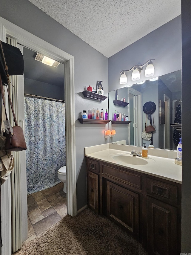 bathroom with toilet, stone finish floor, vanity, and a textured ceiling