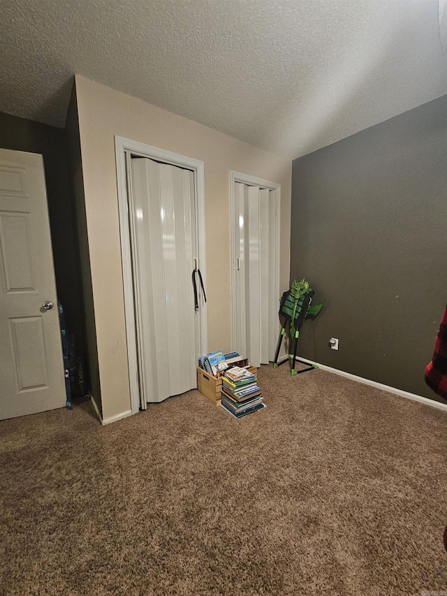 unfurnished bedroom with a textured ceiling, two closets, baseboards, and carpet floors