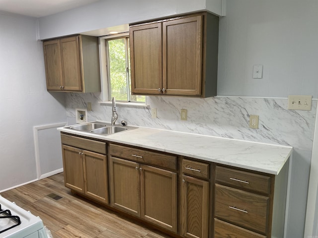 kitchen with visible vents, a sink, light wood-style flooring, and backsplash