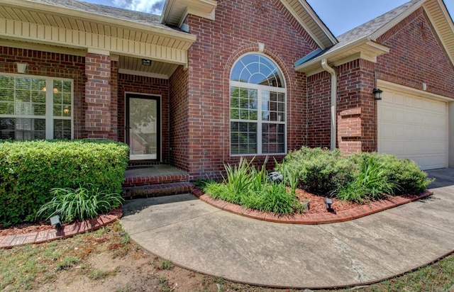 property entrance with brick siding, an attached garage, and driveway