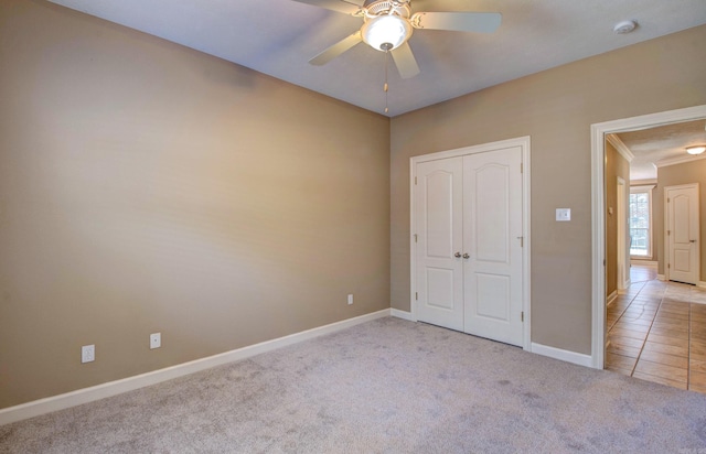 unfurnished bedroom featuring carpet flooring, crown molding, a ceiling fan, baseboards, and a closet