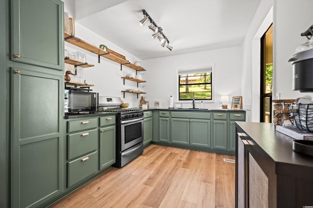 kitchen featuring stainless steel range with gas stovetop, open shelves, a sink, green cabinets, and light wood-style flooring
