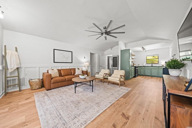 living area featuring ceiling fan, vaulted ceiling, wainscoting, and light wood-style floors