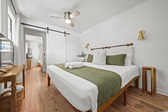 bedroom featuring a ceiling fan, baseboards, a barn door, and wood finished floors