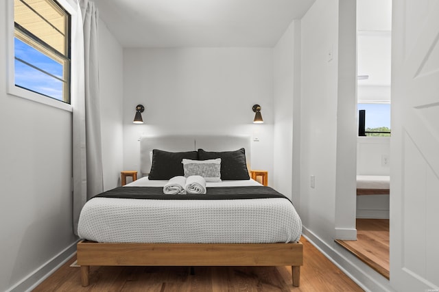 bedroom with baseboards, wood finished floors, and multiple windows