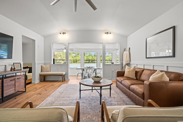 living area with light wood-style floors, a ceiling fan, a wainscoted wall, and vaulted ceiling