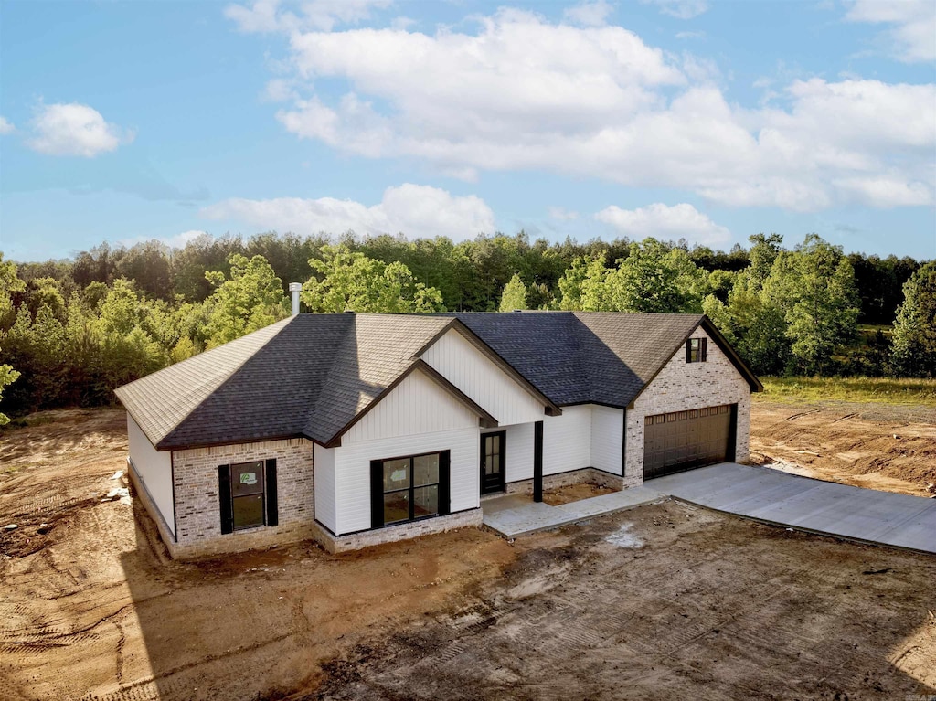 modern inspired farmhouse featuring brick siding, driveway, and roof with shingles
