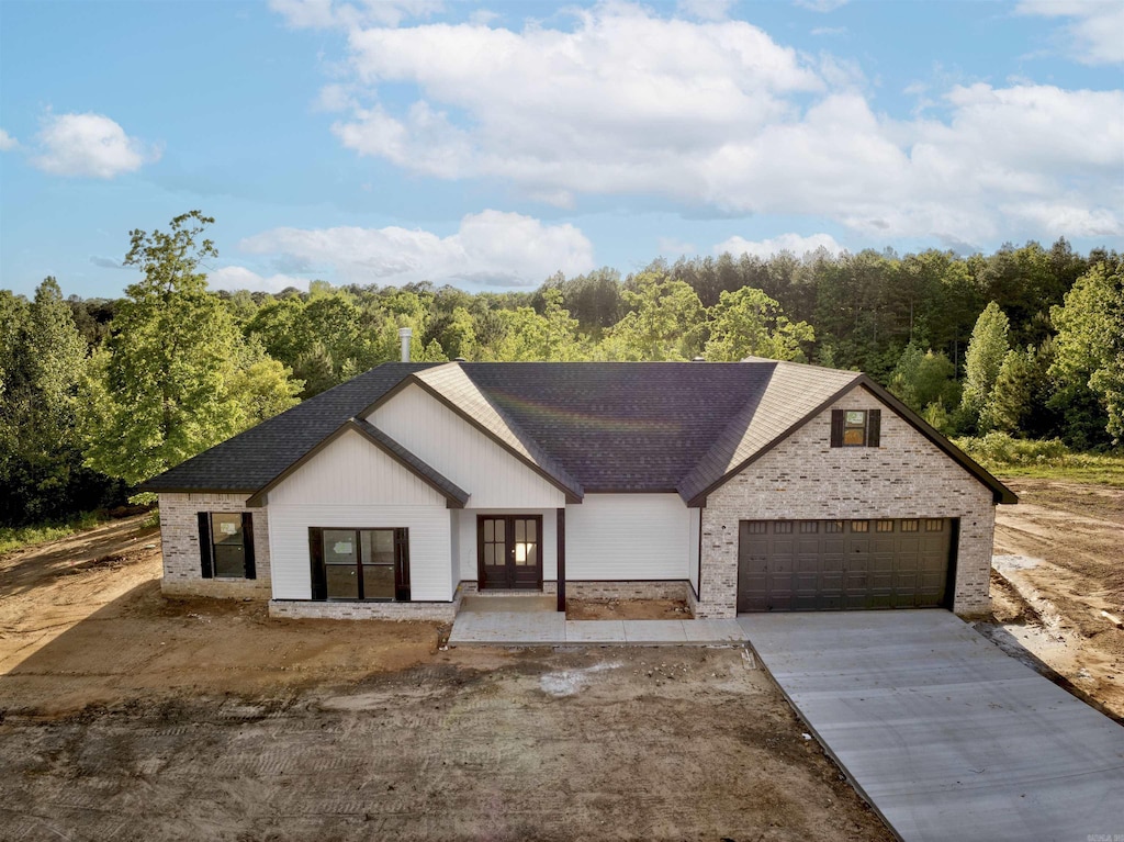 view of front of house with a garage, french doors, a shingled roof, a view of trees, and driveway