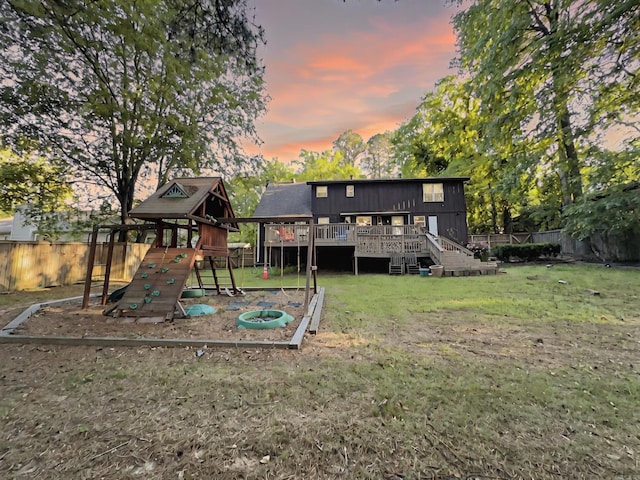 back of property at dusk with a fenced backyard, a playground, a yard, and a deck