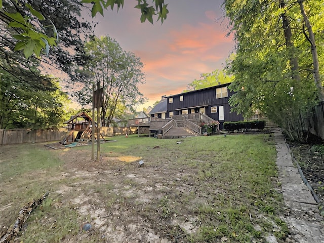 yard at dusk featuring a fenced backyard, a playground, and a deck