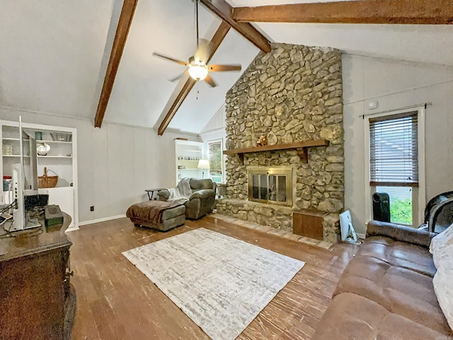 living area with vaulted ceiling with beams, ceiling fan, a stone fireplace, and wood finished floors