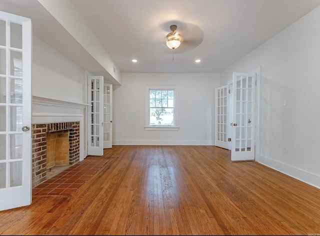 unfurnished living room with a brick fireplace, wood finished floors, baseboards, recessed lighting, and french doors