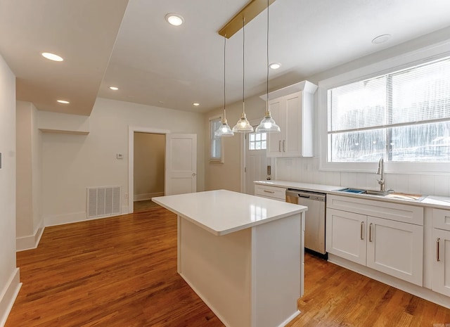 kitchen featuring white cabinets, a sink, a center island, stainless steel dishwasher, and visible vents