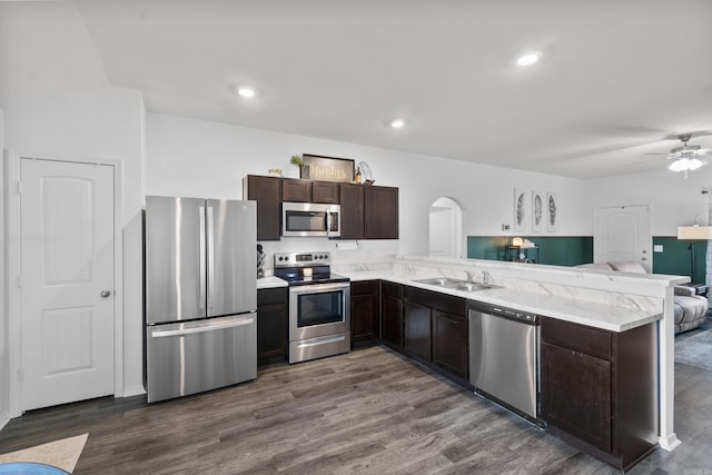 kitchen featuring dark brown cabinetry, appliances with stainless steel finishes, arched walkways, a sink, and open floor plan
