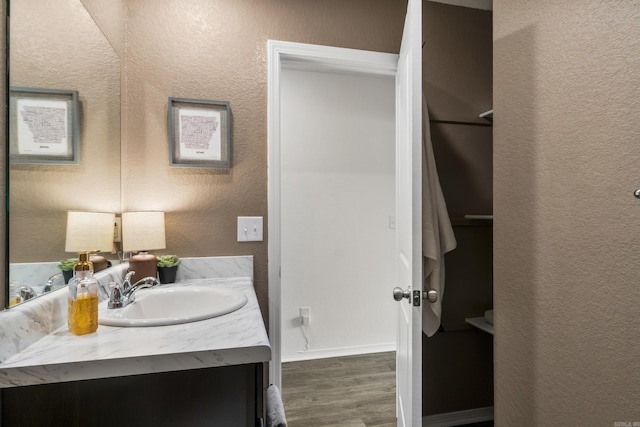 bathroom with vanity, a textured wall, baseboards, and wood finished floors