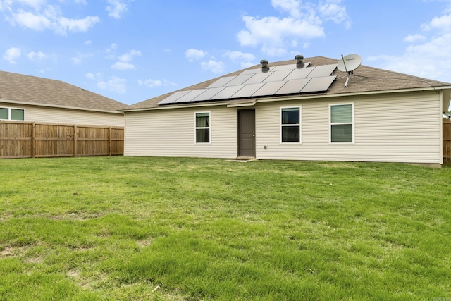 back of property featuring a lawn, roof mounted solar panels, and a fenced backyard