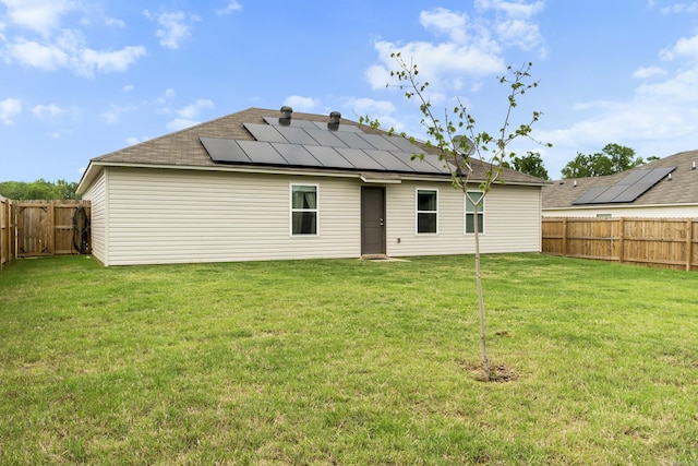 back of house with a fenced backyard, roof mounted solar panels, roof with shingles, and a yard