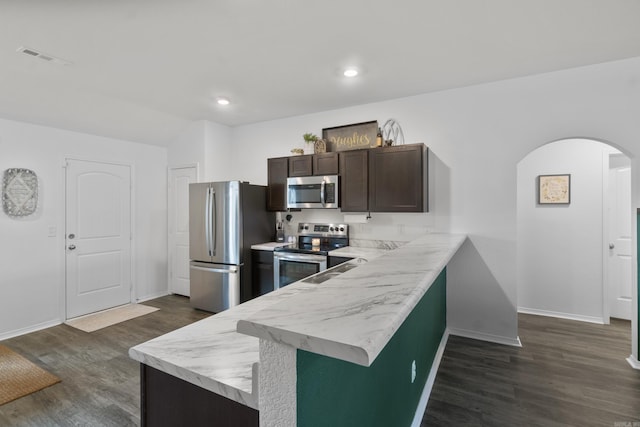kitchen with dark wood-style flooring, dark brown cabinets, light countertops, arched walkways, and stainless steel appliances