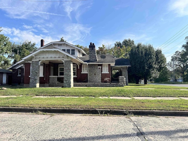 craftsman-style home with brick siding, a front yard, stone siding, and a chimney