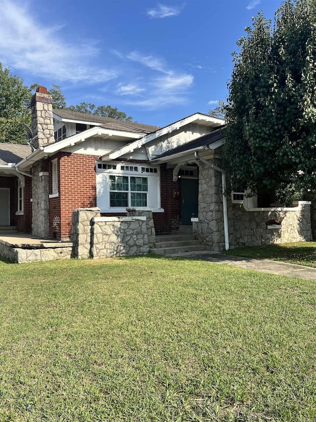 view of front facade with brick siding, a chimney, stone siding, and a front lawn