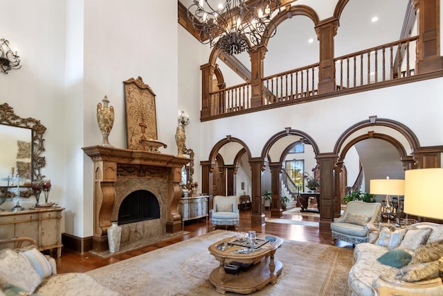 living room with wood finished floors, a towering ceiling, ornate columns, a chandelier, and arched walkways