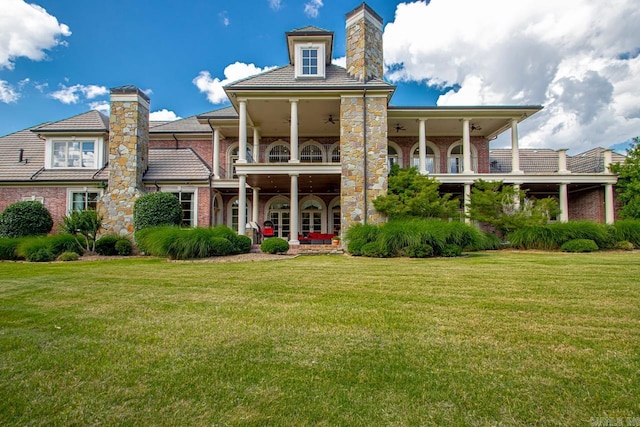 rear view of house featuring a yard, a balcony, a chimney, brick siding, and ceiling fan