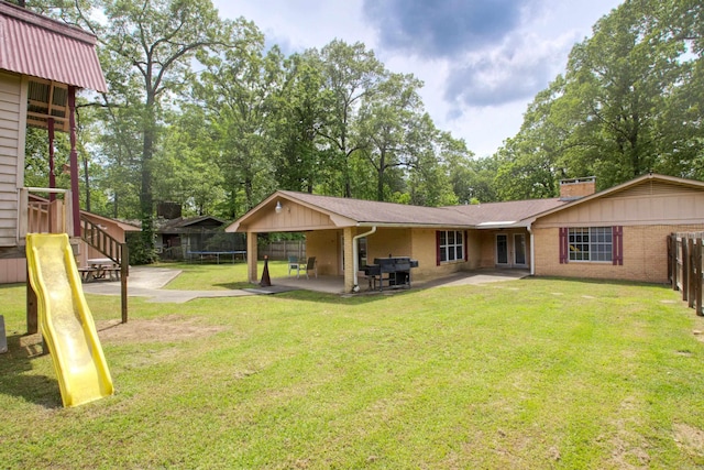 back of house featuring a lawn, a chimney, brick siding, a patio, and a trampoline