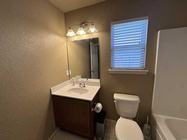 bathroom with toilet, a tub to relax in, baseboards, a textured wall, and vanity