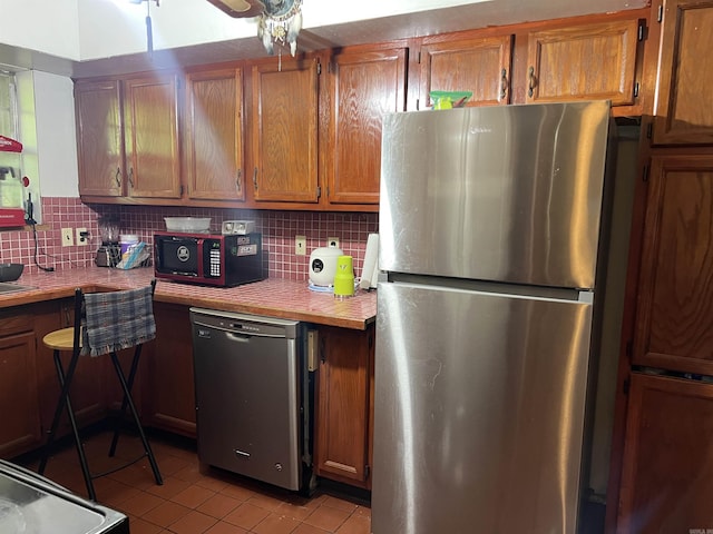 kitchen featuring freestanding refrigerator, light countertops, brown cabinetry, and light tile patterned flooring