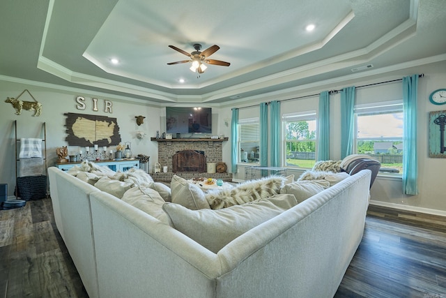 living area featuring a tray ceiling, crown molding, dark wood-type flooring, and a ceiling fan