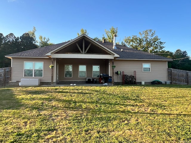 rear view of property featuring fence, a shingled roof, a patio area, and a lawn