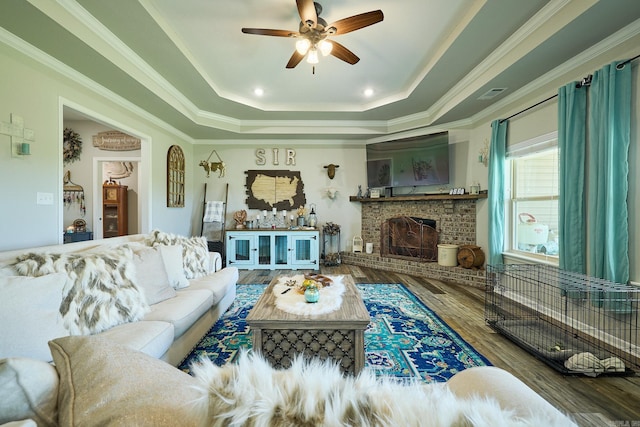 living room featuring wood finished floors, a fireplace, visible vents, a raised ceiling, and ceiling fan