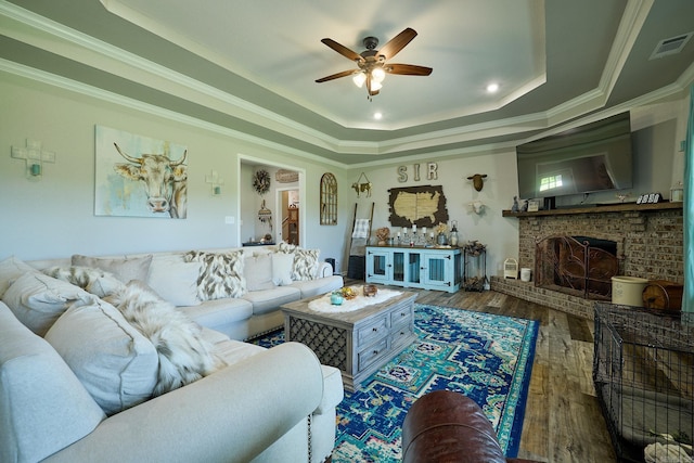 living area with ceiling fan, visible vents, a brick fireplace, wood finished floors, and a raised ceiling