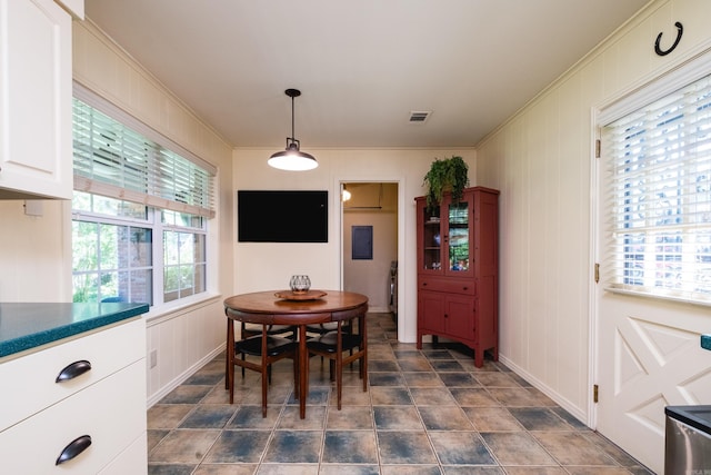 dining area with visible vents, a decorative wall, stone finish flooring, and ornamental molding